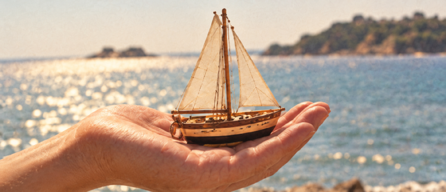 Un voilier miniature au creux d’une main, face a la mer